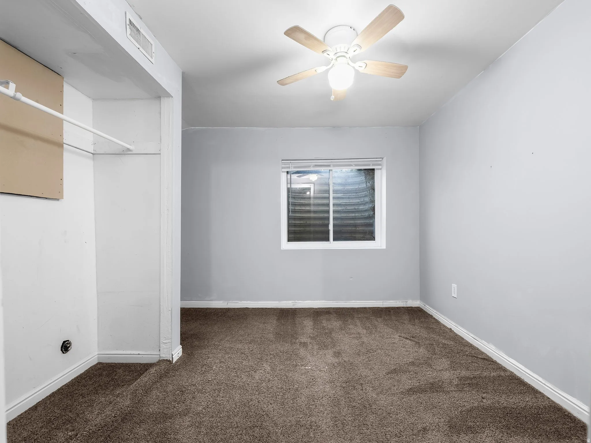 Carpeted room with a ceiling fan, a window, and a built-in closet with a hanging rod