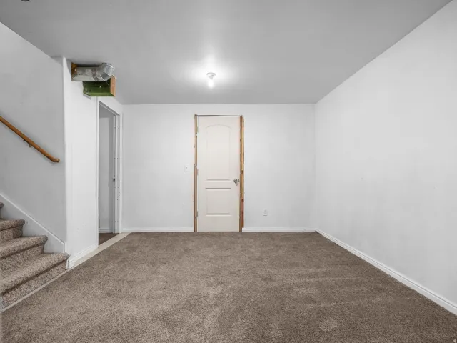 Carpeted flooring, white painted walls, white paneled door, and a wooden handrail
