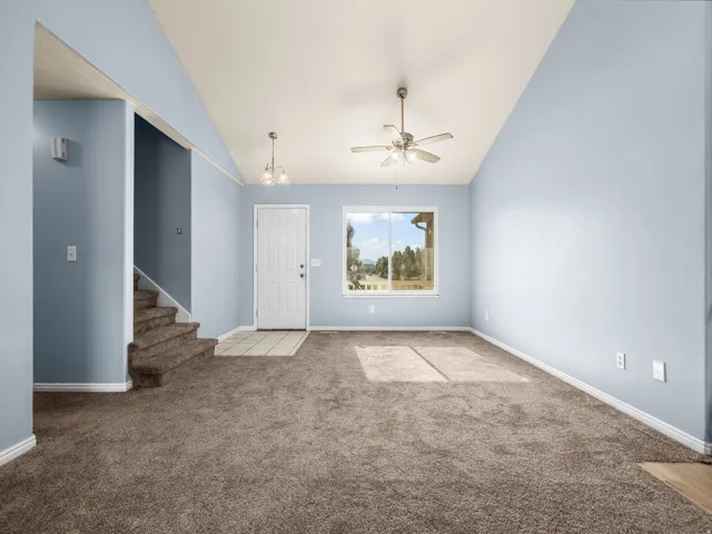 Vaulted ceiling, ceiling fan, white door, window with outdoor scenery, tiled entry