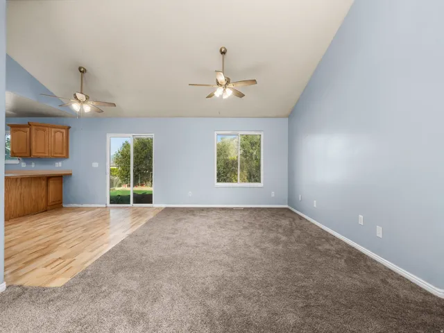 Vaulted ceilings with two ceiling fans, mixed flooring with wood-finish and carpet, sliding glass door, and a window providing exterior views