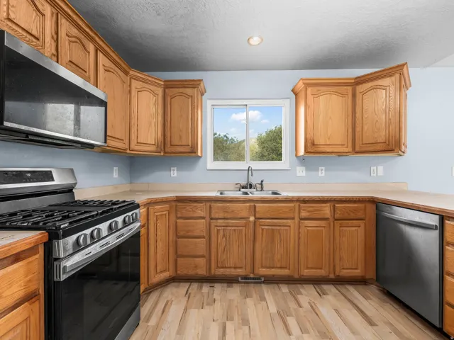 Kitchen featuring wood cabinetry, stainless steel appliances, a double basin sink, and wood-finish flooring
