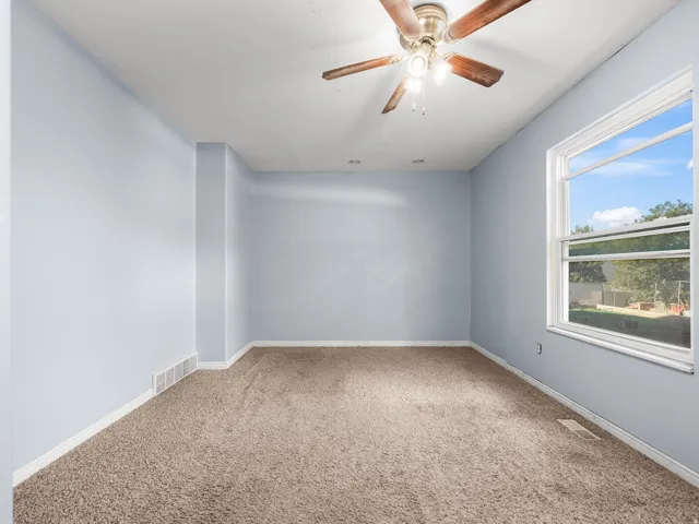 Ceiling fan with wood-finish blades, large window, and carpeted flooring