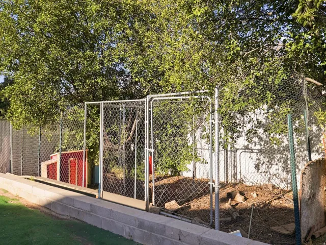 Chain-link fencing with a gate, concrete block retaining wall, and mature trees