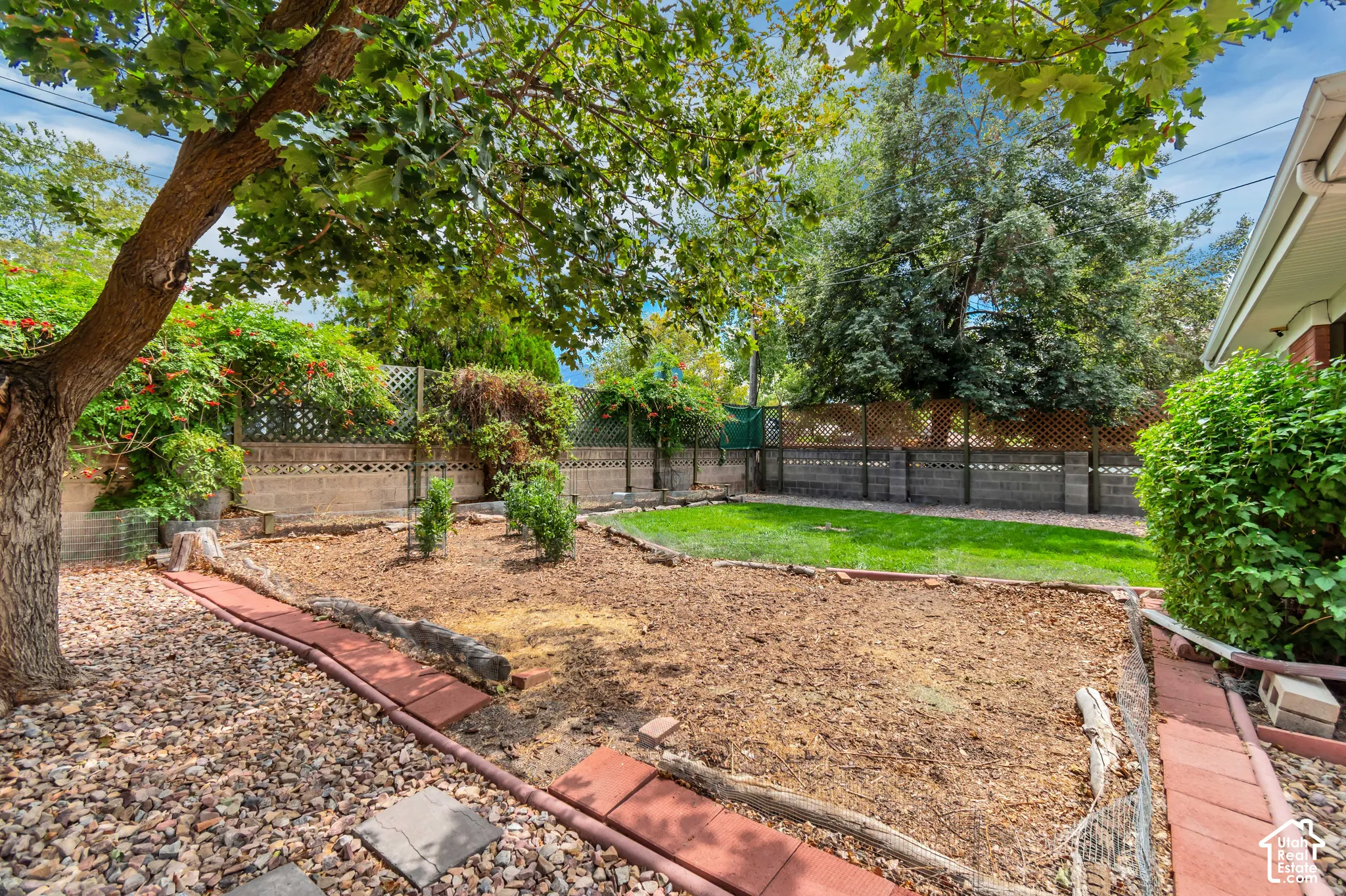 Private backyard with a manicured lawn, established landscaping, decorative rock accents, and a block and lattice fence