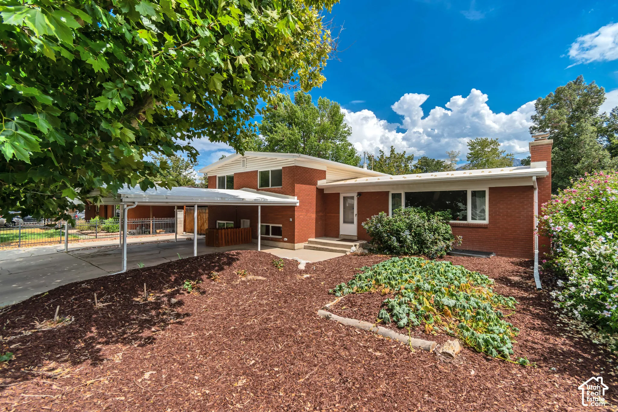 Brick exterior, carport, mature trees, landscaped front yard, and a covered entry