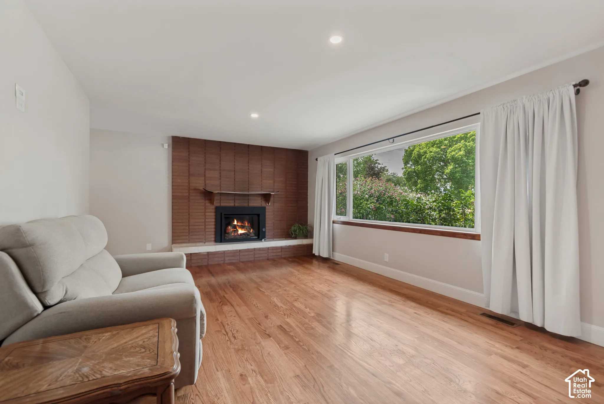 Brick-finish fireplace with a stone hearth, recessed lighting, and wood-finish flooring