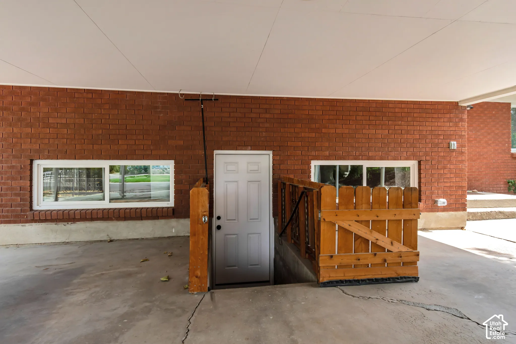Private entrance to the Mother-In-Law apartment. Brick exterior with white-framed windows, a covered concrete patio, and a wood entry gate