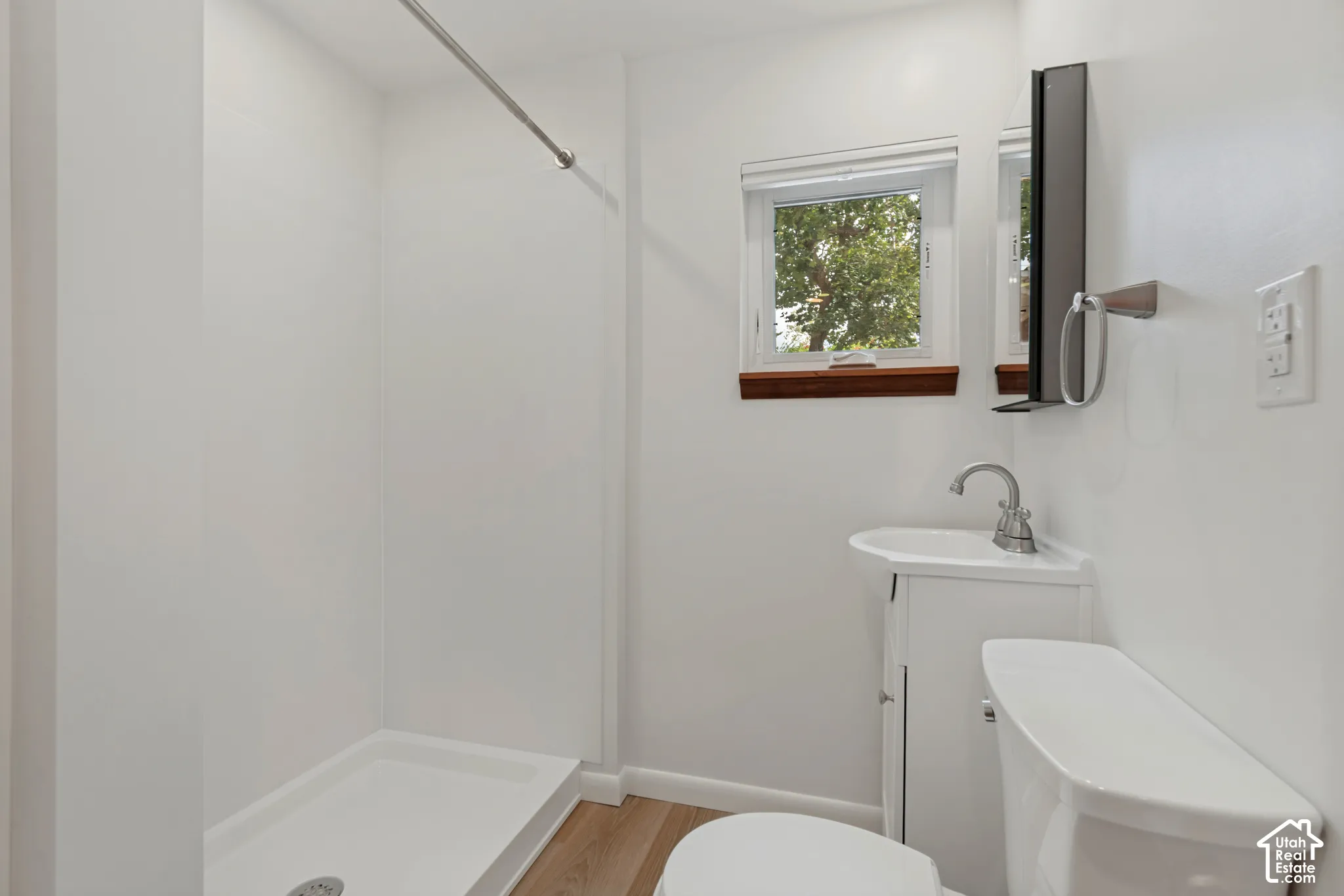 Shower stall with white surround, vanity with integrated sink, chrome faucet, wall-mounted mirror, linen storage, medicine cabinet storage and wood-finish flooring
