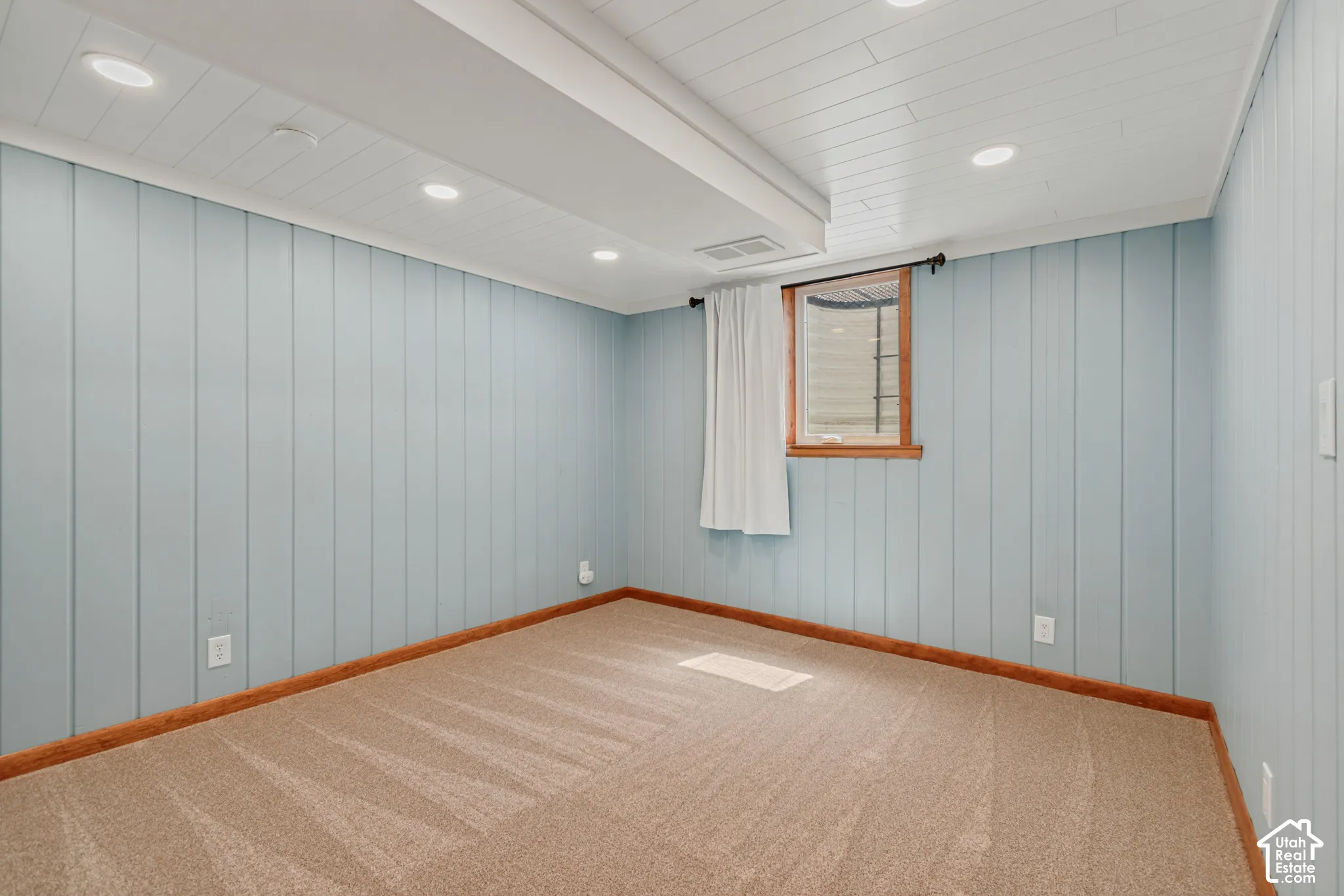 Vertical paneled wall finish, recessed ceiling lighting, light-toned carpeting, and a wood-framed window. Den/gaming room/office for basement bedroom 1