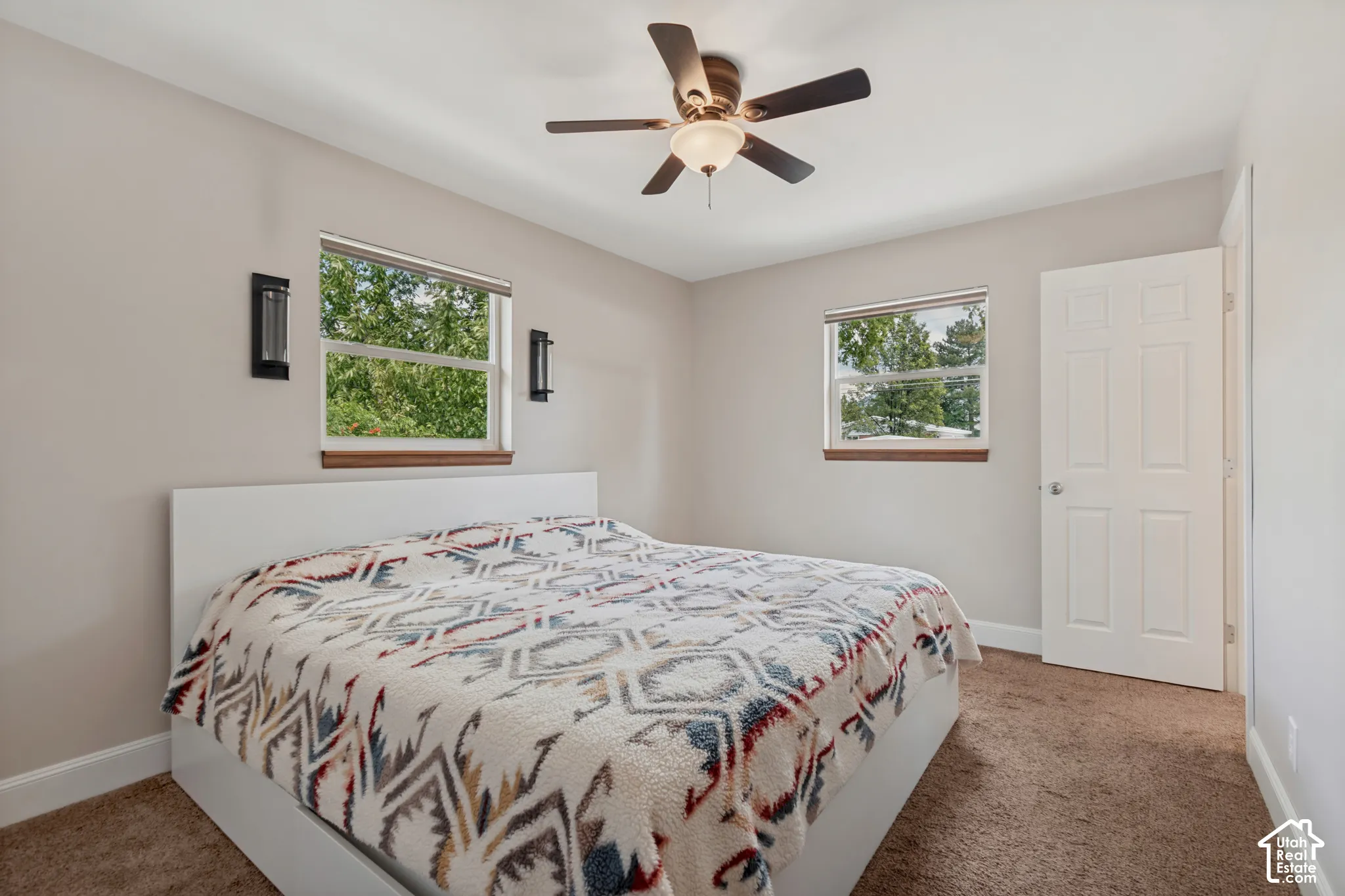 Primary bedroom with a ceiling fan, dual windows, wall-mounted sconces, and private bathroom