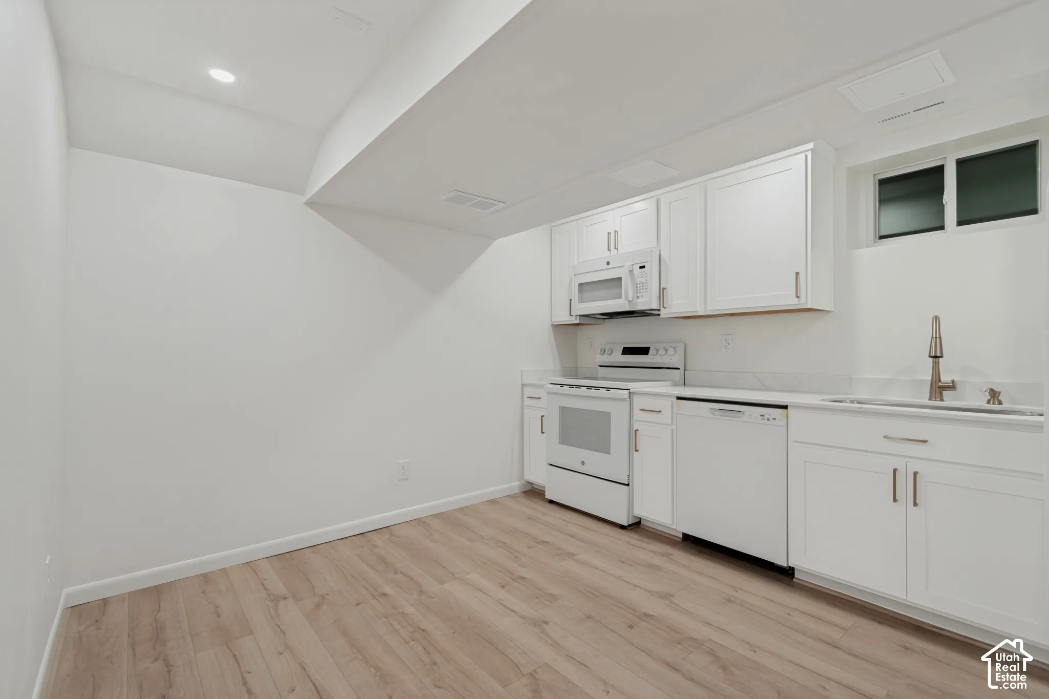 White cabinetry, stainless steel sink with pull-down faucet, white appliances, recessed lighting, and wood-finish flooring. Mother-In-Law Apartment