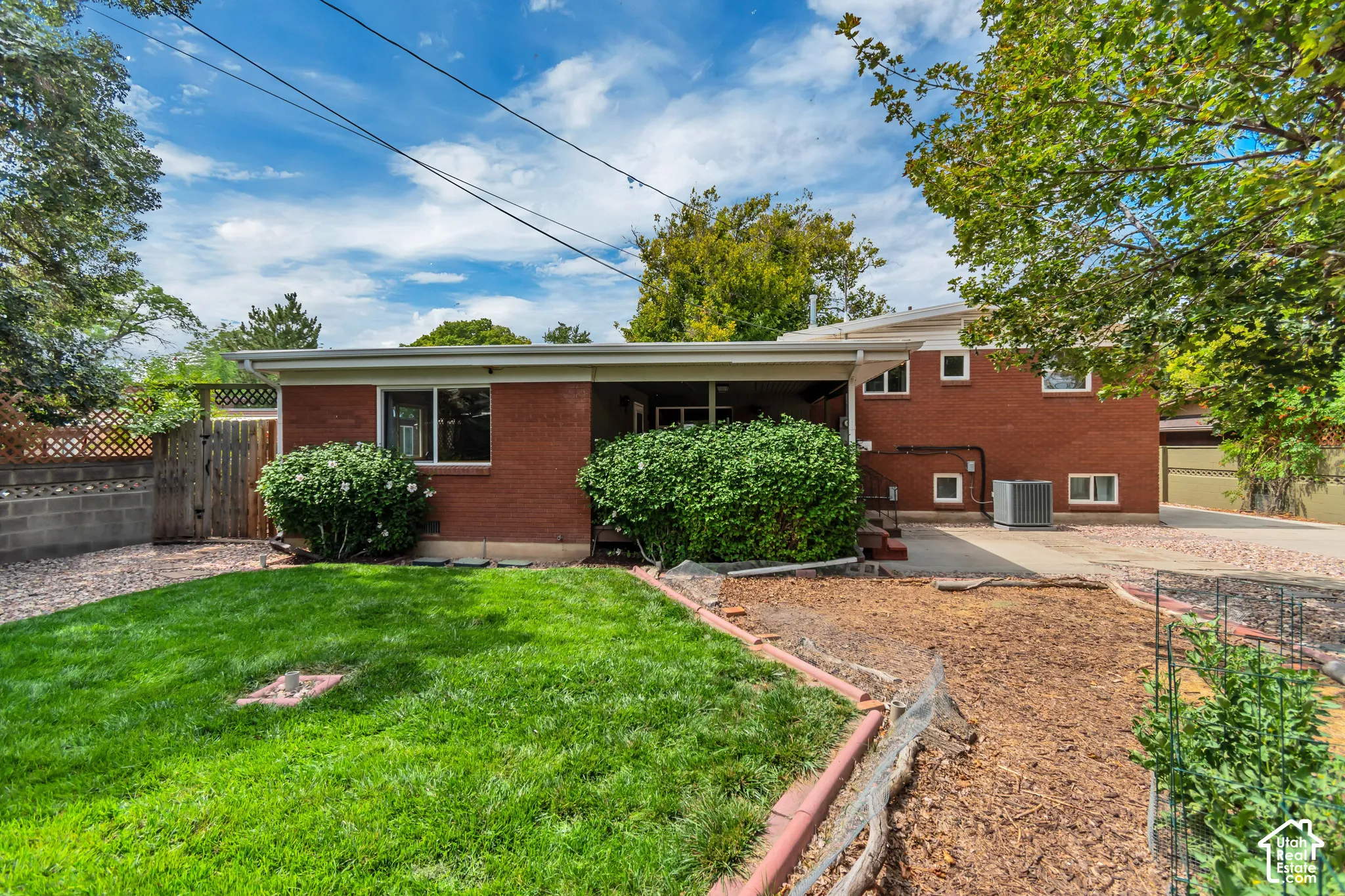 Brick exterior with white trim, covered patio, manicured lawn, established landscaping, and a wood privacy fence. Fenced in dog run located on the left side of the yard
