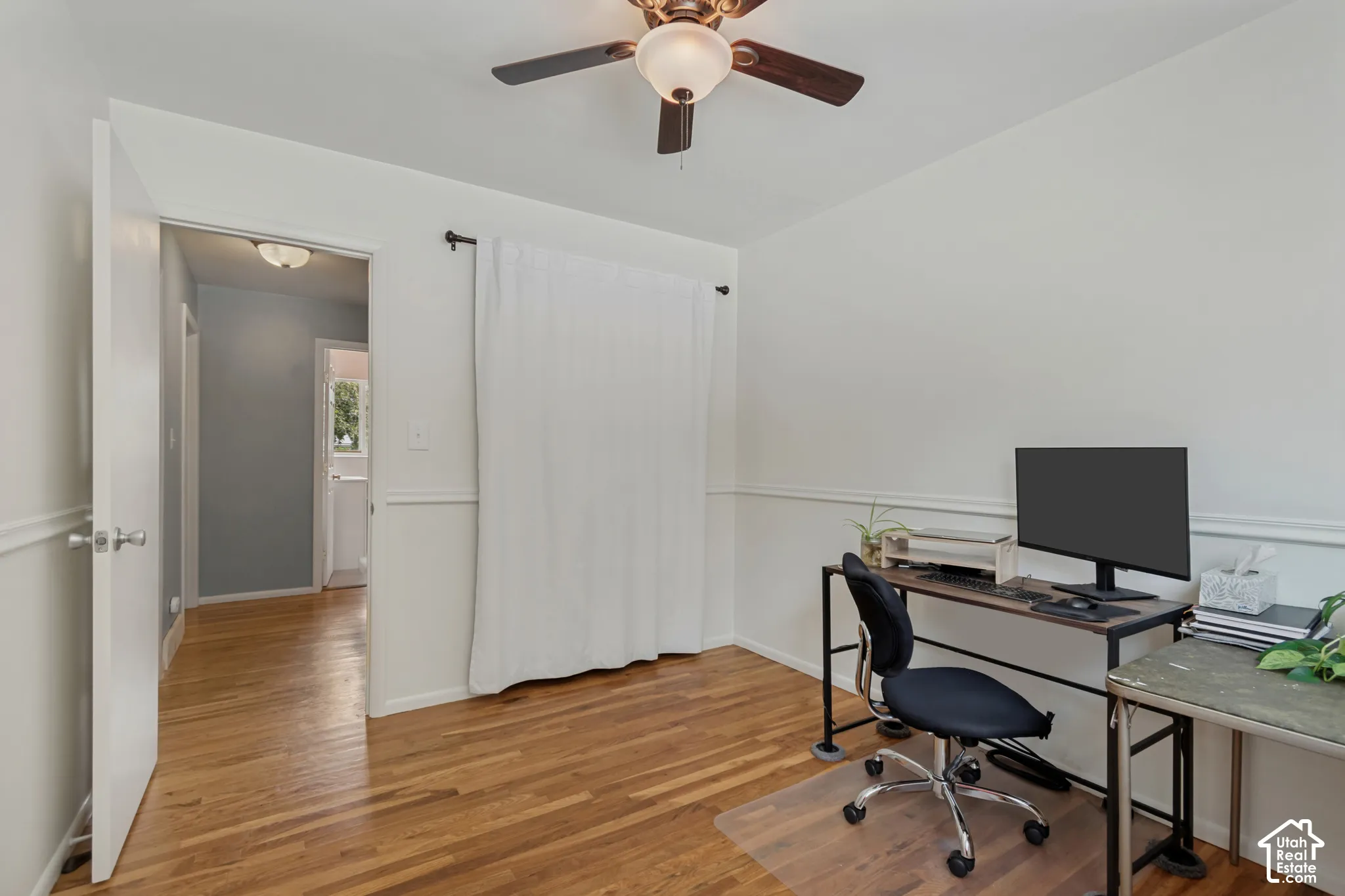 Spacious home office/bedroom featuring hardwood flooring, ceiling fan with integrated lighting, and chair rail detail