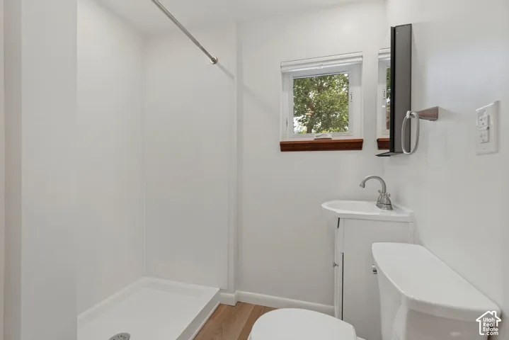 Shower stall with white surround, vanity with integrated sink, chrome faucet, wall-mounted mirror, linen storage, medicine cabinet storage and wood-finish flooring