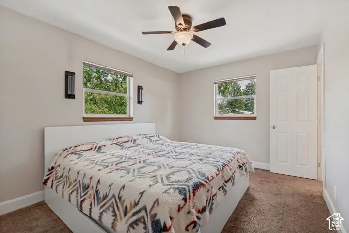 Primary bedroom with a ceiling fan, dual windows, wall-mounted sconces, and private bathroom