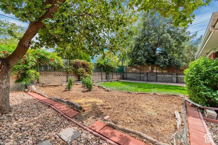Private backyard with a manicured lawn, established landscaping, decorative rock accents, and a block and lattice fence