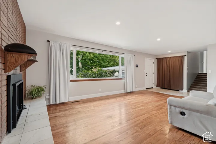 Large picture window, brick-faced fireplace with a tile hearth, wood-finish flooring, and recessed lighting
