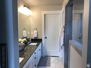 Dual vanity with under-mount sinks, dark granite countertops, and white cabinetry
