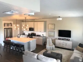 Open-concept living space featuring a kitchen island with seating, stainless steel appliances, white cabinetry, and wood-finish flooring