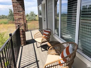 Outdoor balcony featuring a brick pillar, dark metal railings, and a light-toned decking surface