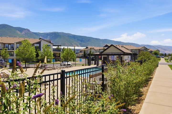 Community swimming pool with a black metal fence, surrounded by green landscaping and a paved walkway