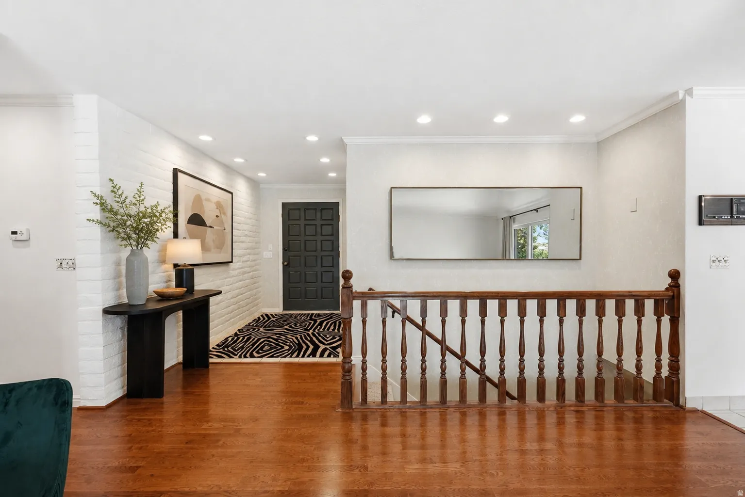 Hardwood flooring, painted brick accent wall, recessed lighting, wood staircase with balusters, and a paneled entry door
