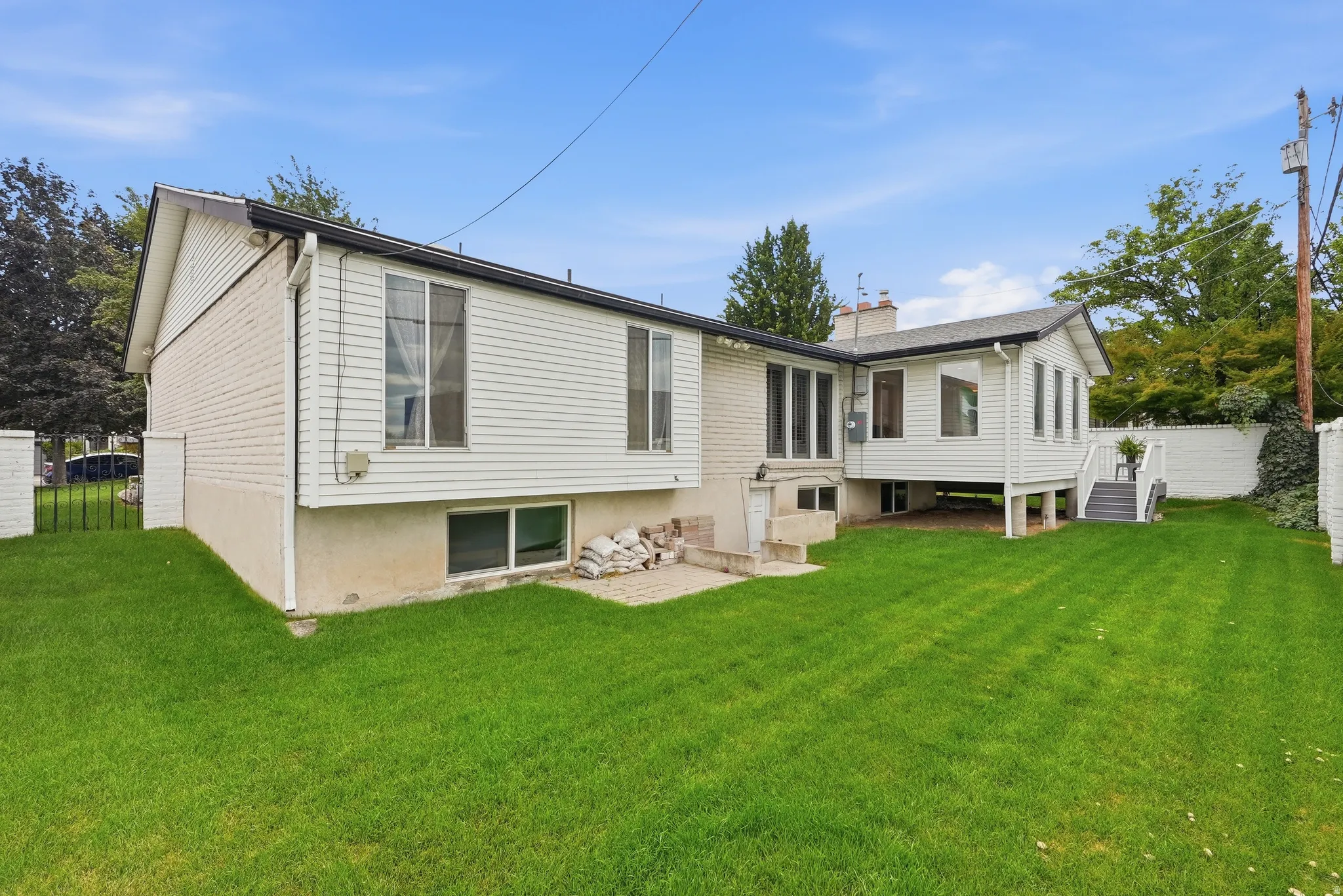 Expansive green lawn, white horizontal siding, brick accent walls, and a multi-level deck with stairs
