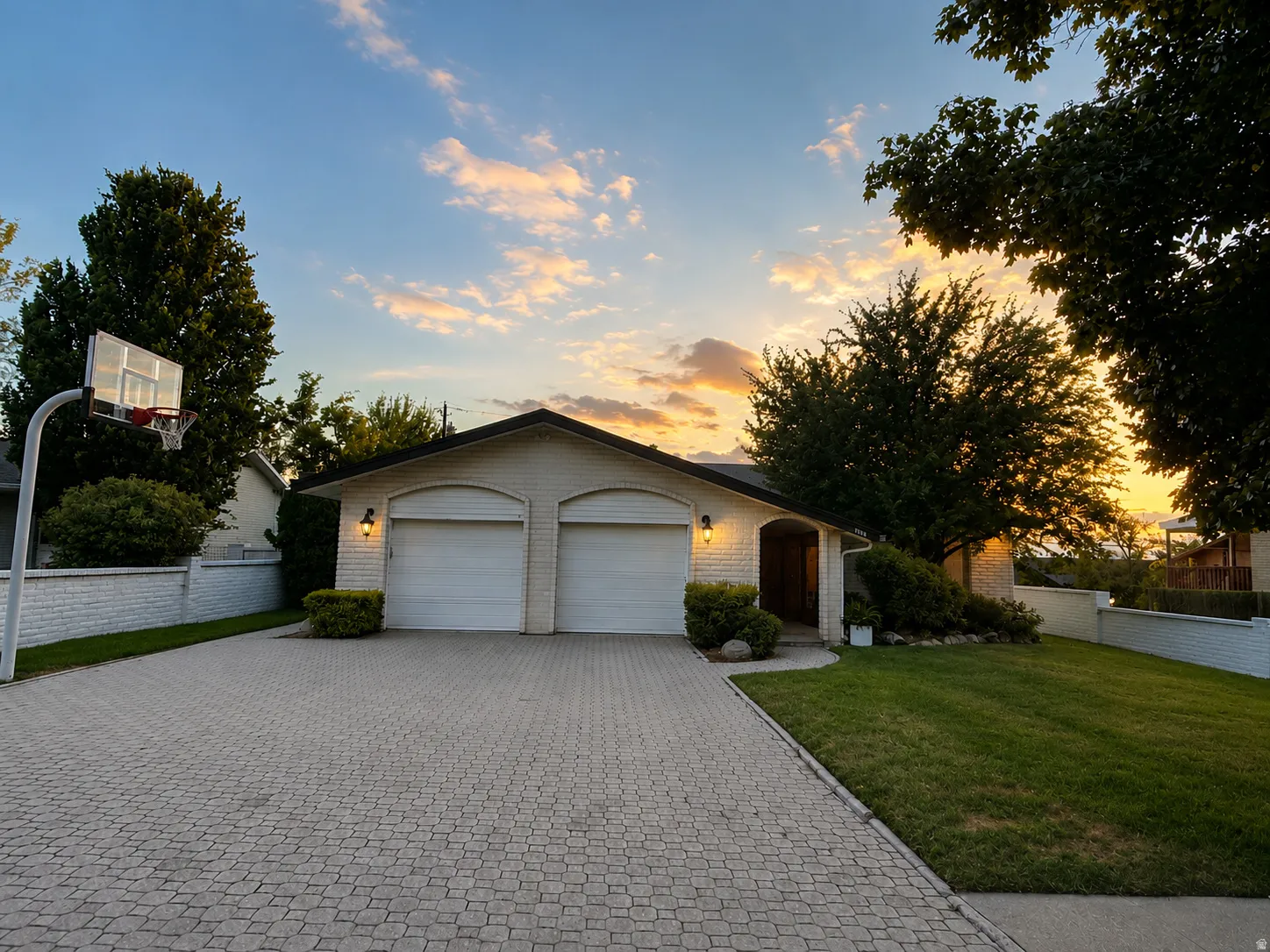 White brick exterior with a two-car garage, extensive paver driveway, and established landscaping