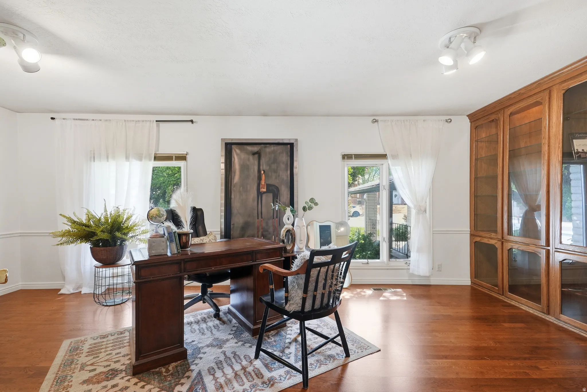 Wood-finish flooring, white walls with wainscoting, and a built-in wooden cabinet with glass doors