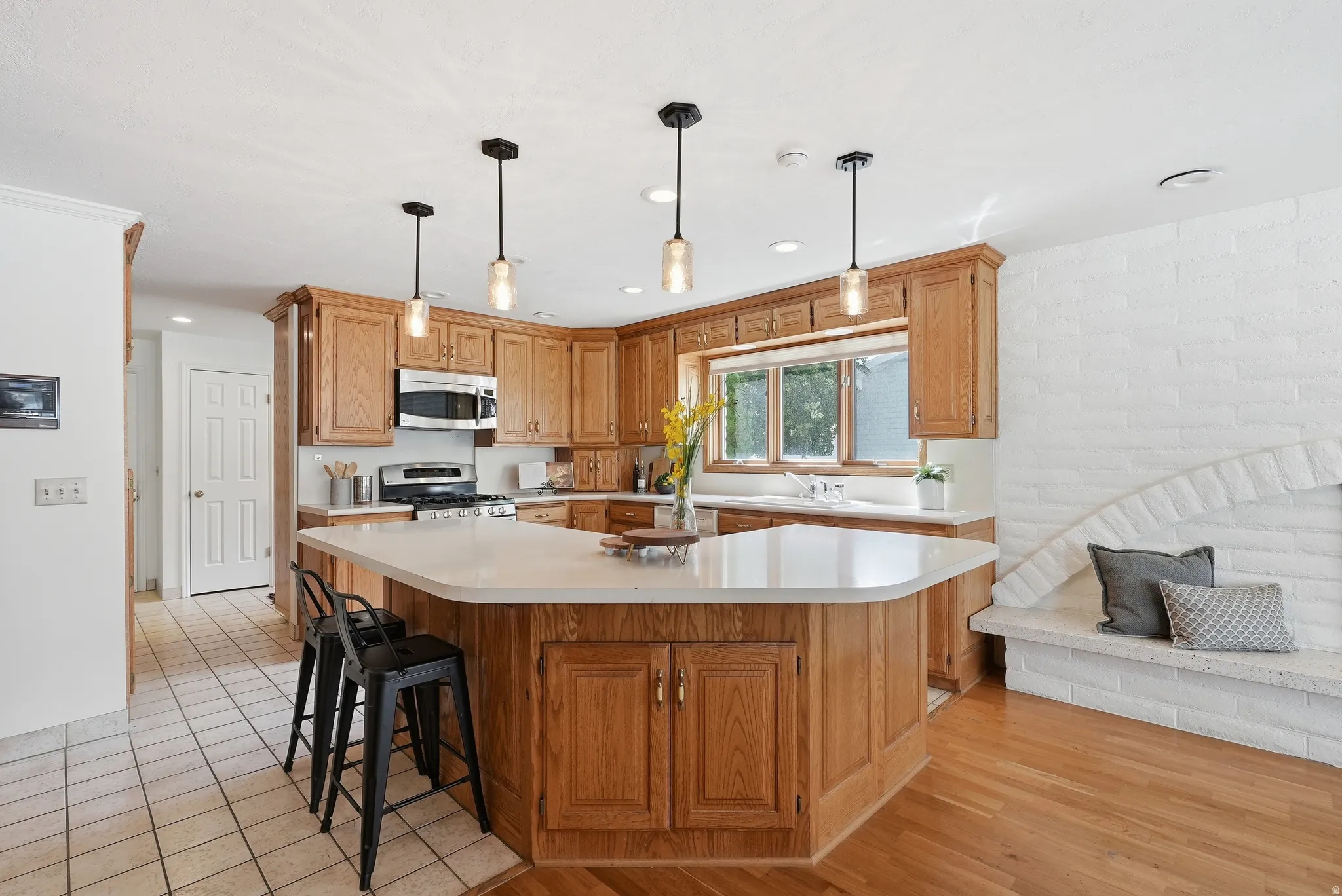Kitchen featuring wood cabinetry, stainless steel appliances, a center island with a light-toned countertop, pendant lighting, and a window above the sink