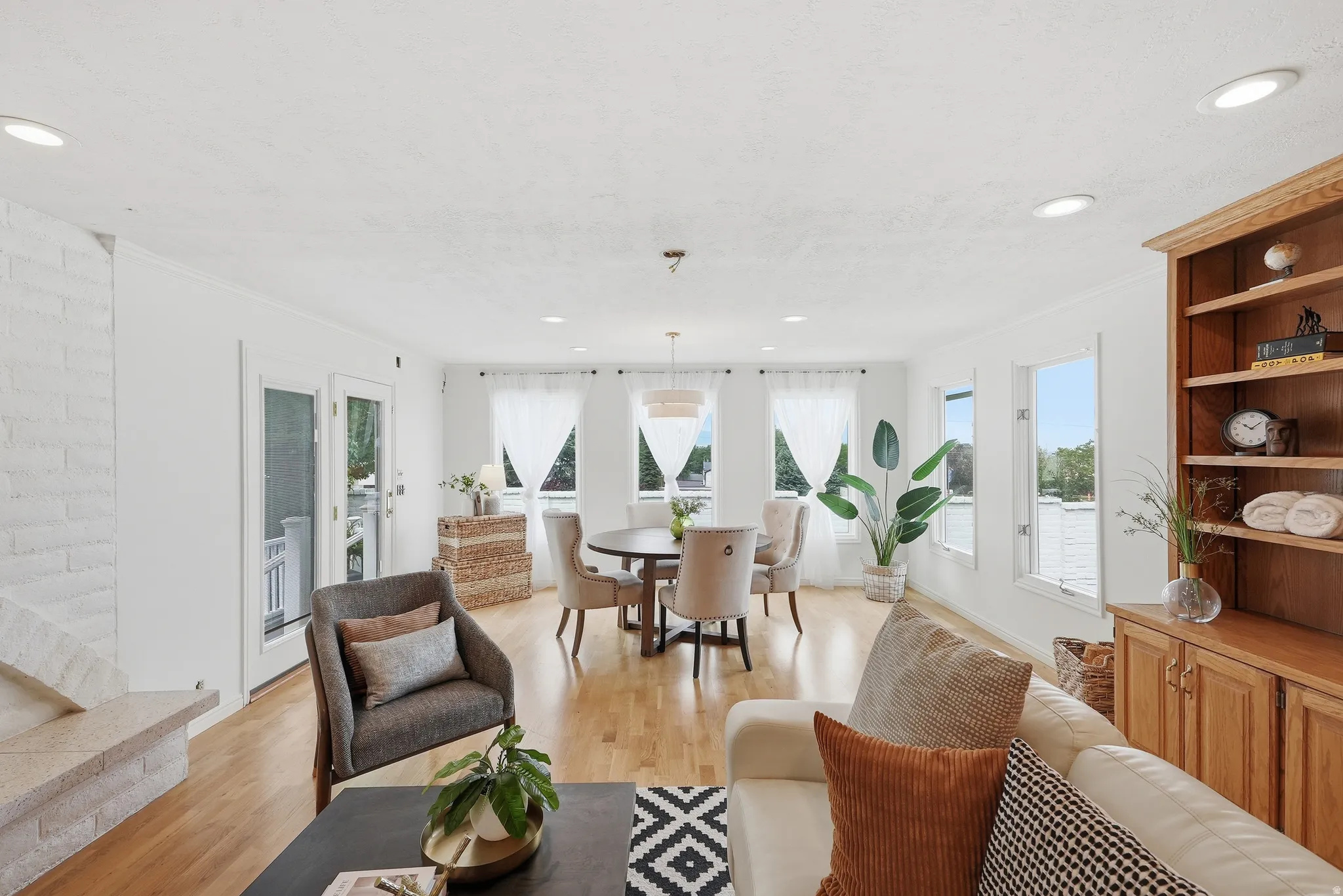 Hardwood flooring throughout, recessed lighting, built-in shelving, white brick fireplace, and multiple windows