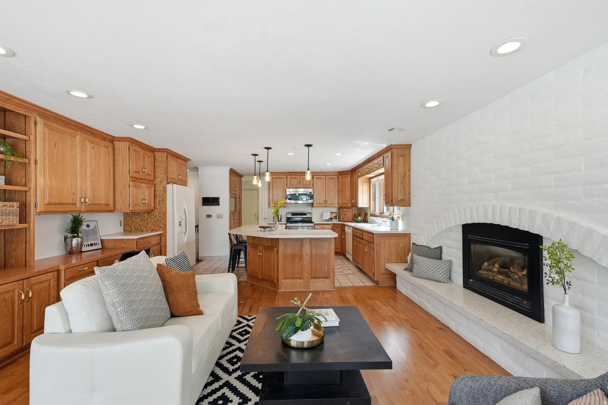 Open-concept living area with wood-finish flooring, a white brick fireplace, and recessed lighting