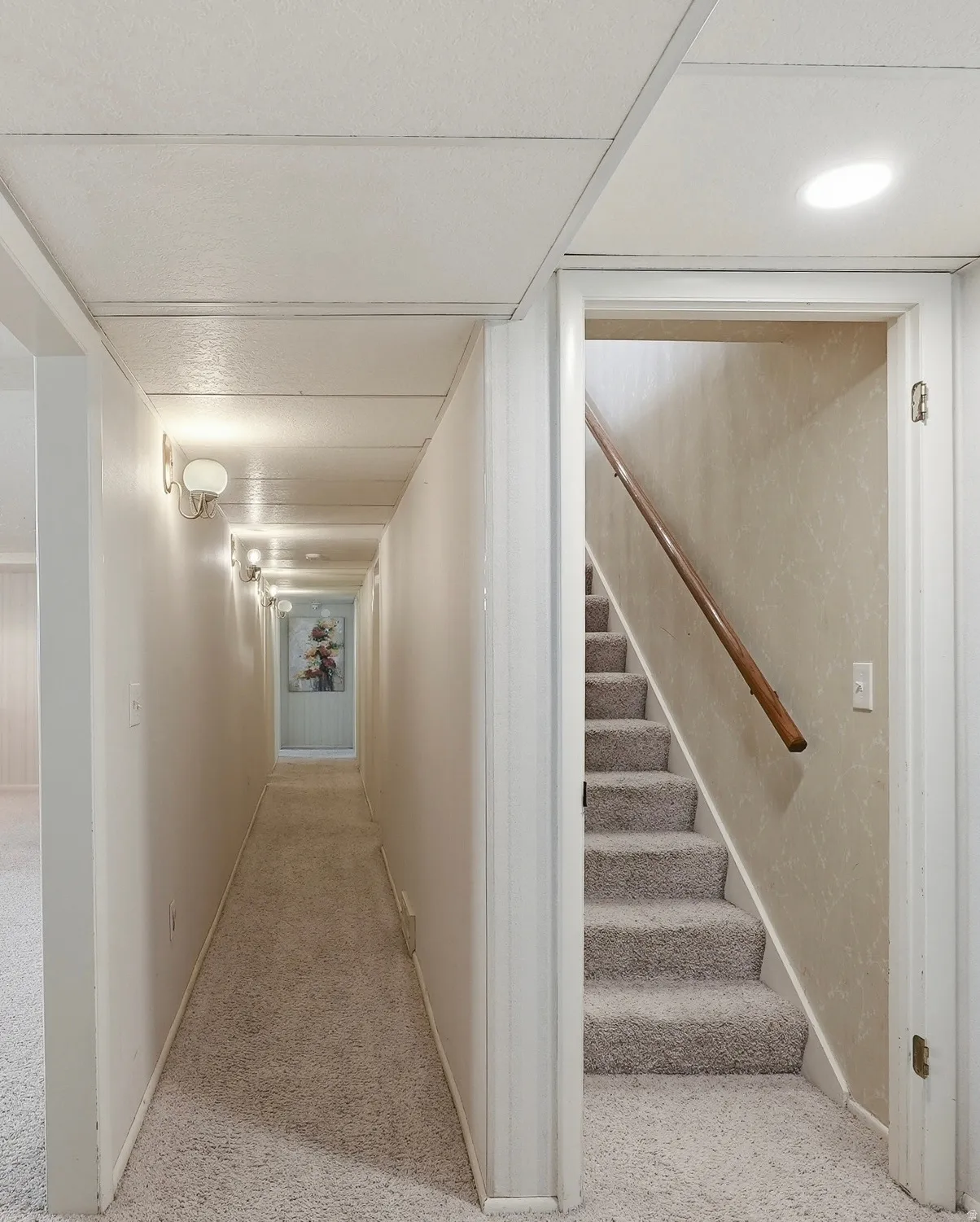 Carpeted flooring throughout, recessed ceiling lighting, wall-mounted light fixtures, and a wooden handrail