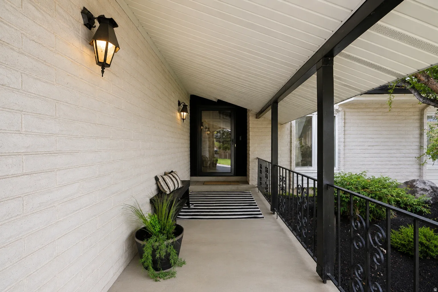 Covered entry with white brick siding, black wrought iron railing, and two exterior sconces