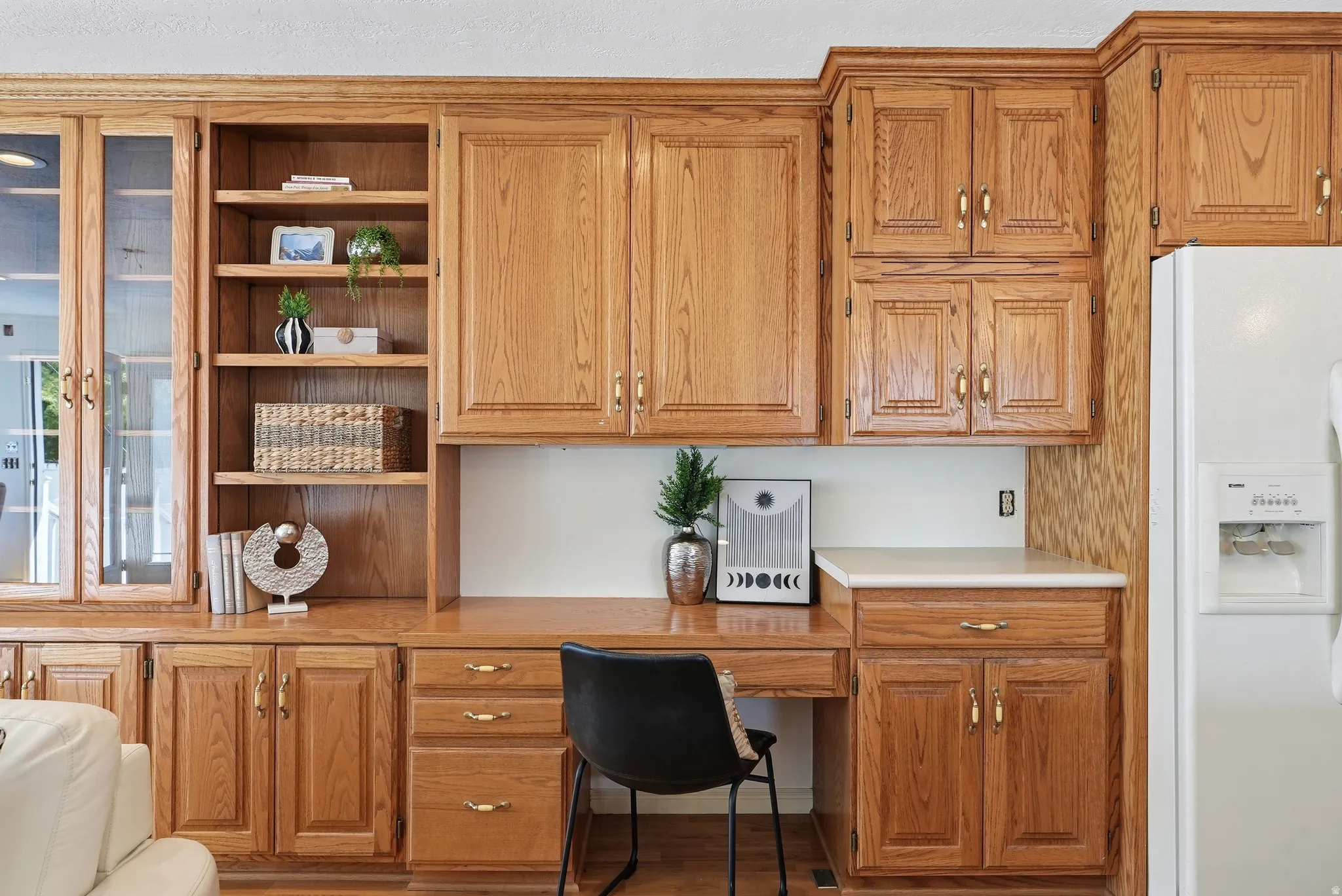 Built-in wood-finish cabinetry, integrated desk space, upper and lower storage, glass-front display cabinets, and neutral countertops