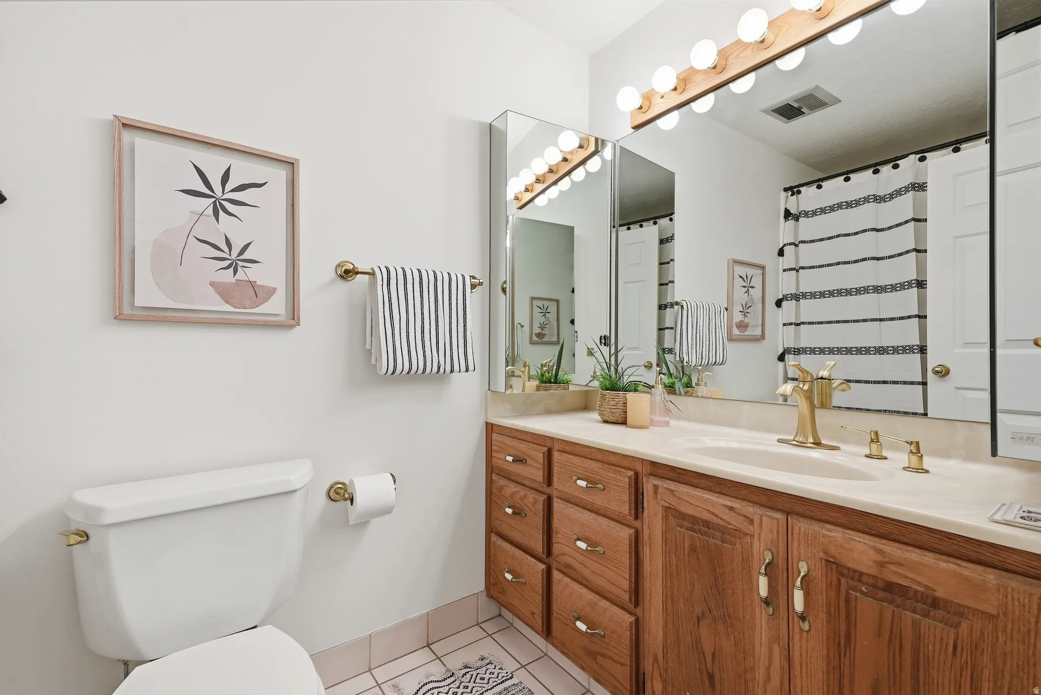 Light-toned wood vanity with ample storage, integrated sink, and brass-finish fixtures