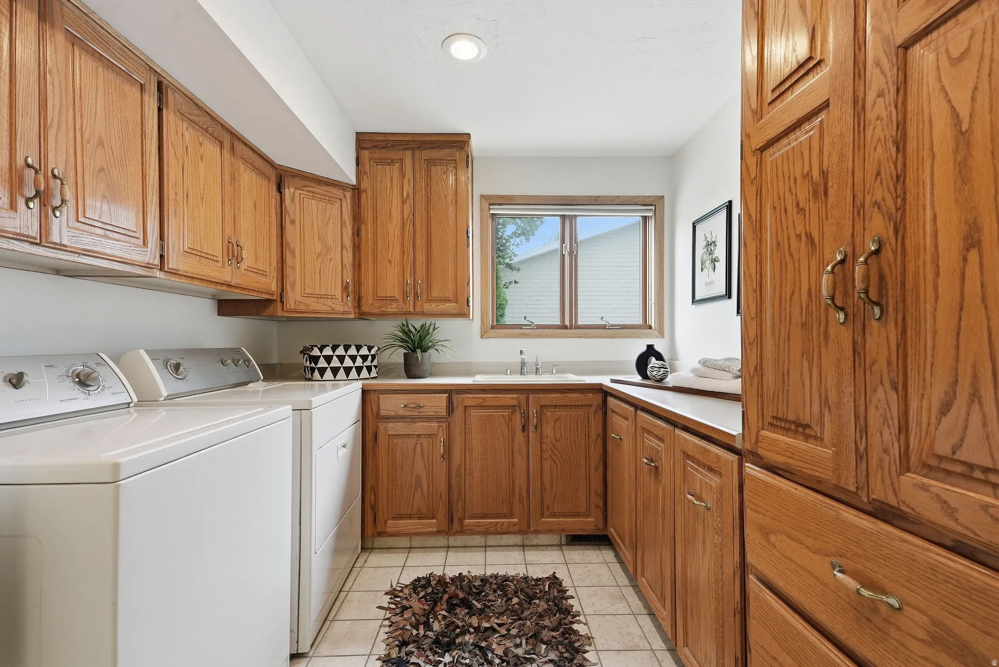 Extensive wood cabinetry, sink basin, white tile flooring, and overhead lighting