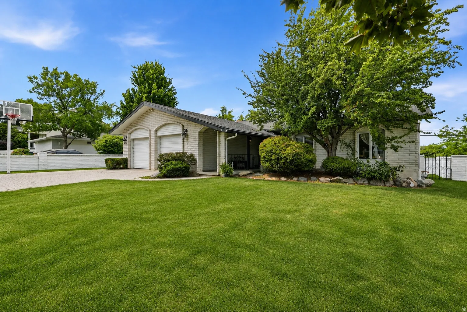 White brick exterior with a two-car garage, established landscaping, and a paved driveway