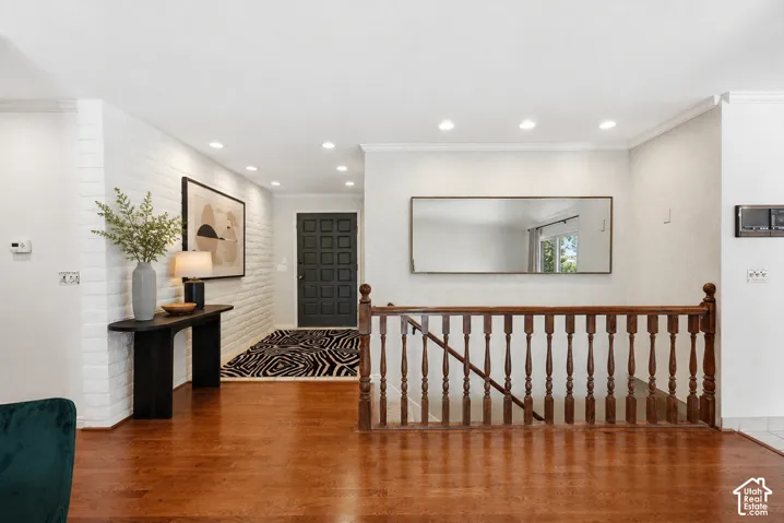 Hardwood flooring, painted brick accent wall, recessed lighting, wood staircase with balusters, and a paneled entry door