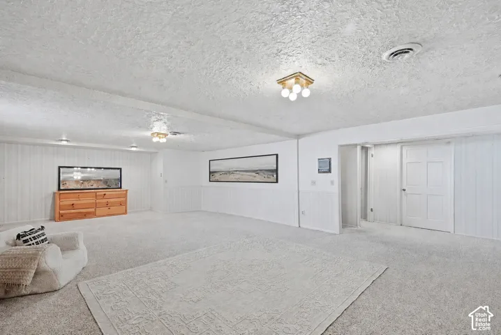 Spacious room featuring light-colored carpeting, white paneled walls, and multiple ceiling light fixtures