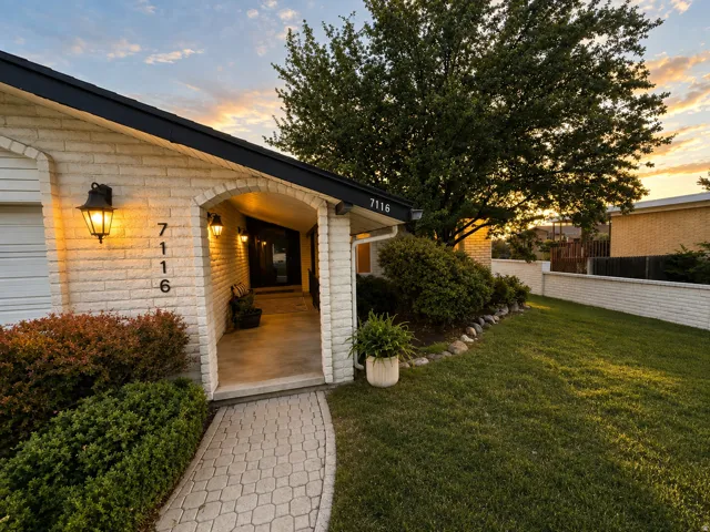 White brick exterior with black trim, an arched entryway, exterior wall sconces, a paver walkway, and mature landscaping