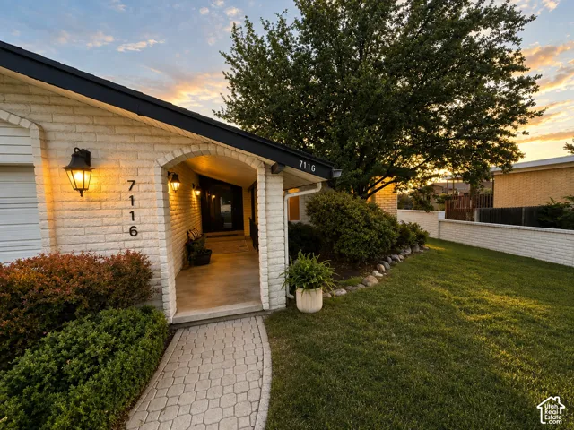 White brick exterior with black trim, an arched entryway, exterior wall sconces, a paver walkway, and mature landscaping