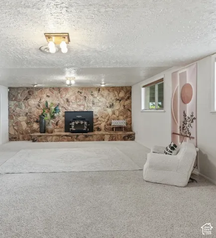Stone accent wall with wood-burning stove, wall-mounted light fixtures, multiple windows, and light-toned carpeting throughout