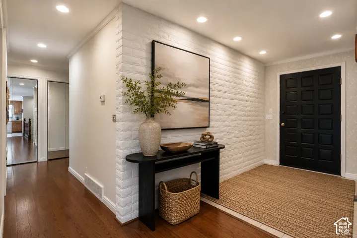 Entryway featuring brick-textured accent wall, recessed lighting, dark wood-finish flooring, and paneled entry door