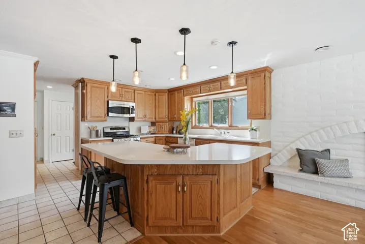 Kitchen featuring wood cabinetry, stainless steel appliances, a center island with a light-toned countertop, pendant lighting, and a window above the sink