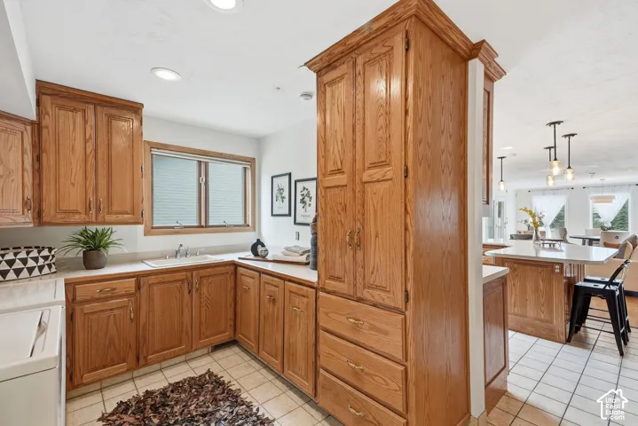 Wood-finish cabinetry with abundant storage, white countertops, built-in sink with faucet, recessed lighting, and tiled flooring
