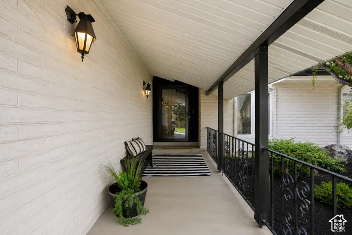 Covered entry with white brick siding, black wrought iron railing, and two exterior sconces