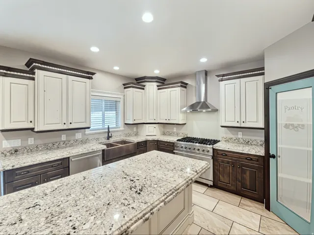 Kitchen featuring an oversized island, dual-tone cabinetry, Viking gas range with hood, copper farmhouse sink, and granite countertops