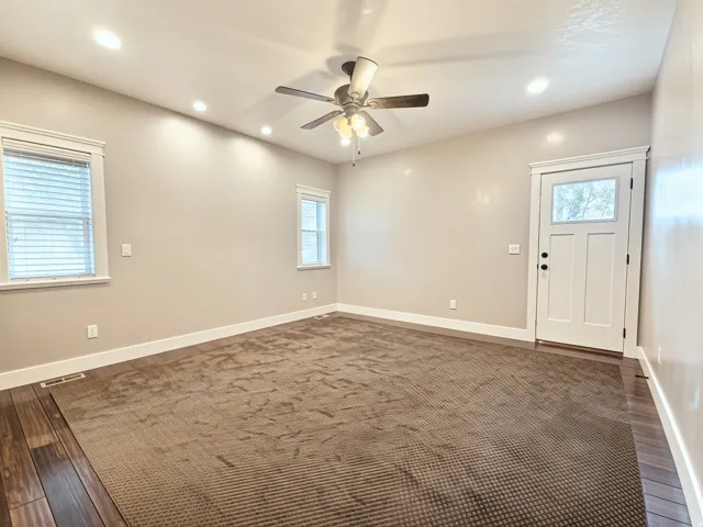 Spacious main floor Primary Bedroom featuring recessed lighting, ceiling fan fixture, wood-finish flooring, two windows with blinds, and an exterior door leading to the backyard patio.