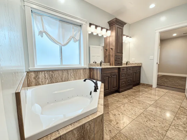Expansive Primary Suite with tiled flooring, a built-in jetted tub, and a double vanity with custom cabinets and copper sinks.